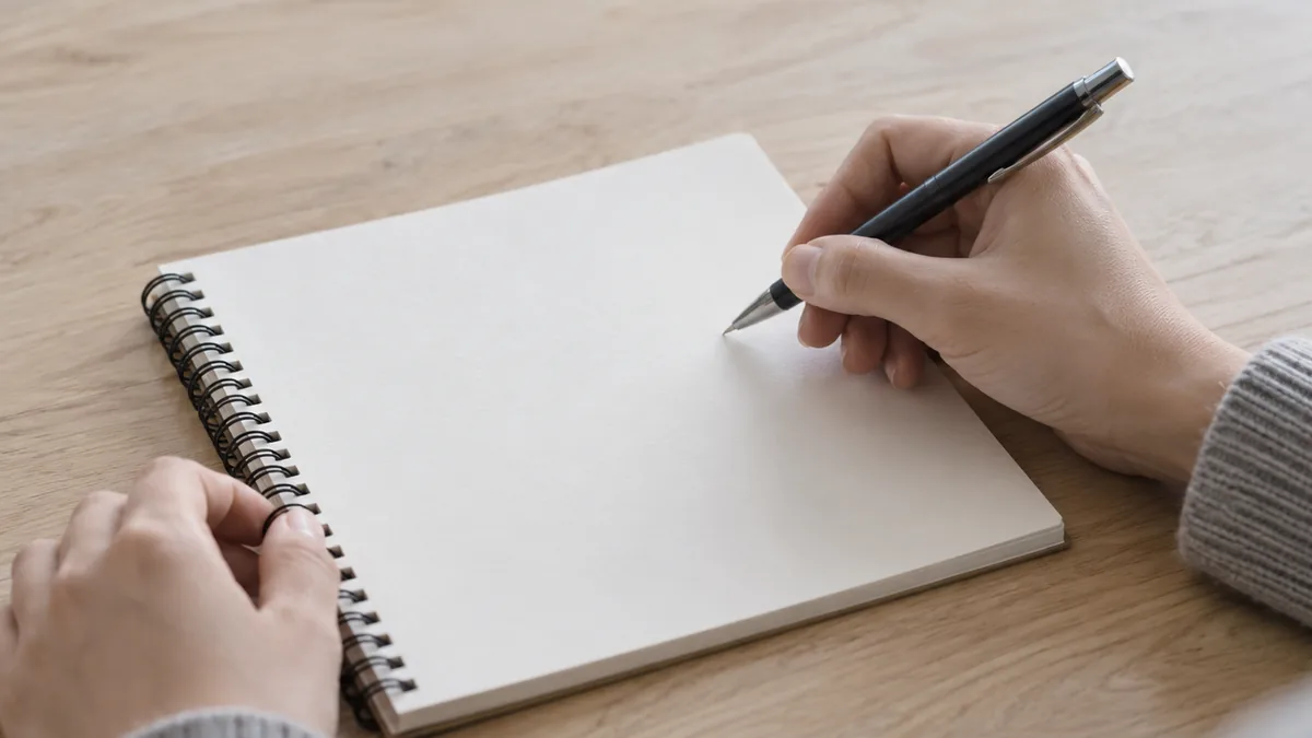 白紙のノートの上でペンを持ち、書く準備をする両手