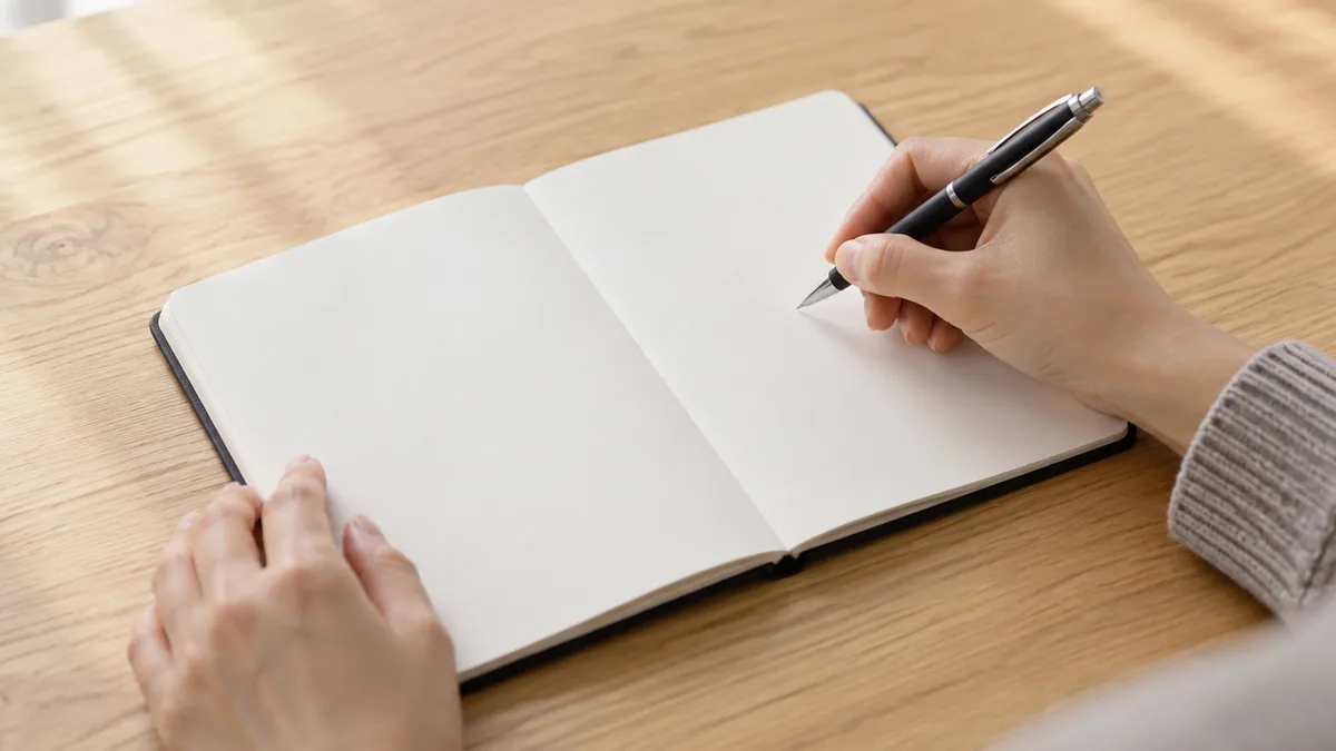 白紙のノートの上でペンを持ち、書く準備をする両手