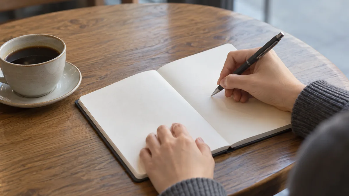 カフェのテーブルで白紙のノートにメモを書く手